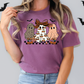 A woman wearing a purple t-shirt with a graphic design of three ghostly figures, including a leopard-print ghost, a checkered ghost, and a pumpkin-wearing ghost.