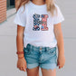 a little girl standing on a sidewalk wearing a t - shirt with the letter h