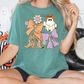 A woman wearing a green t-shirt with a graphic of a ghost, bow, and boots, sitting on a couch with Halloween decorations in the background.