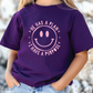 A person wearing a purple t-shirt with a smiley face design and text printed on it.