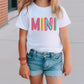 a little girl wearing a white shirt with the word mini on it