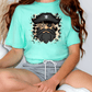 A person wearing a turquoise t-shirt with a pirate-themed graphic and gray shorts is sitting on the floor.
