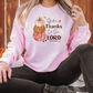 a woman sitting on the ground wearing a pink thanksgiving sweatshirt