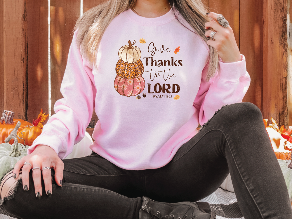 a woman sitting on the ground wearing a pink thanksgiving sweatshirt