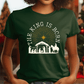 A woman wearing a green t-shirt with a graphic design depicting a nativity scene and the text "The King is Born" printed on it.