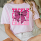 a woman sitting on a bed wearing a pink shirt