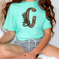 A person wearing a mint green t-shirt with a leopard print design and gray shorts is sitting on the floor.