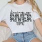 a woman sitting on a couch wearing a white shirt that says living on river time