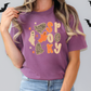 A woman wearing a purple t-shirt with a Halloween-themed design, including a ghost, a leopard print, and the word "Spooky" written on it.