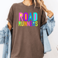 A person wearing a brown t-shirt with the text "ROAD RUNNERS" in colorful letters, along with a denim jacket, stands against a white background.