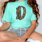 A person wearing a turquoise t-shirt with a leopard print design and gray shorts is sitting on the floor.