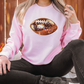 a woman sitting on the ground wearing a pink sweatshirt with a football on it