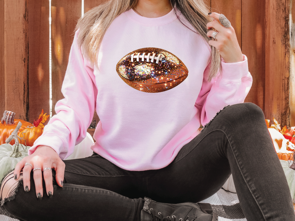 a woman sitting on the ground wearing a pink sweatshirt with a football on it