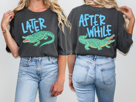 two women wearing black t-shirts with a graphic of a green alligator on the back. The t-shirts have the text "later" and "after while" printed on them.