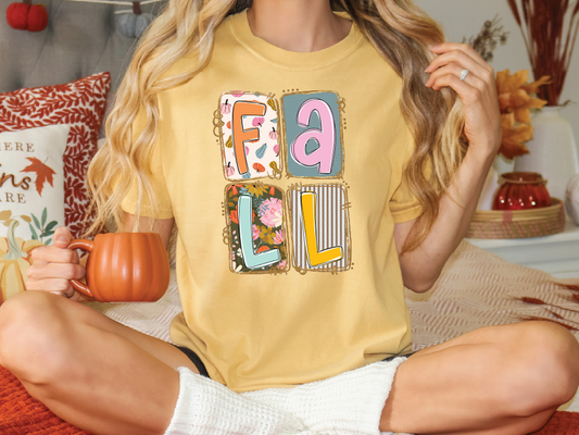 A woman wearing a yellow t-shirt with the word "FALL" printed on it, sitting on a bed with a pumpkin-shaped mug in her hand.