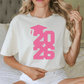 A woman wearing a white t-shirt with a pink graduation cap and the number "2026" printed on it.