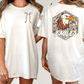 two different views of a white t-shirt with a graphic design on the back. The design features an eagle head with a camouflage pattern and the word "EAGLES" written below it.