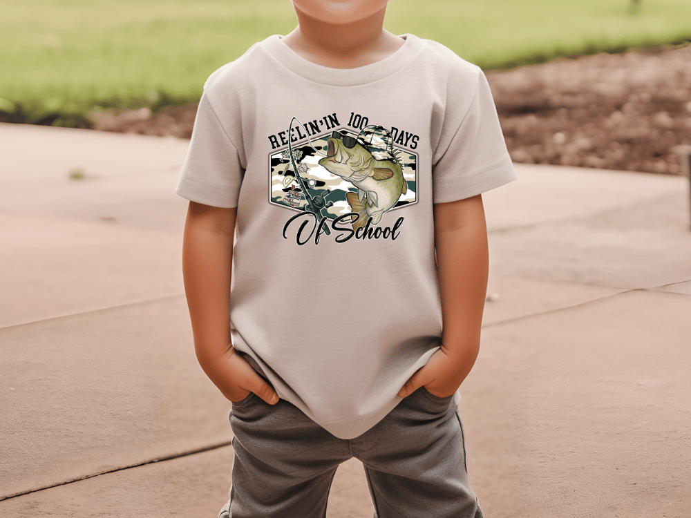 A child wearing a t-shirt with a graphic design featuring a fish and the text "REELIN' IN JOY - DAYS OF SCHOOL".