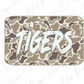 A camouflage-patterned rectangular object with the word "TIGERS" written in bold, white brushstrokes on it.