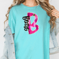 A woman wearing a turquoise t-shirt with a pink and black design on it, and a denim jacket.