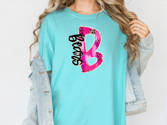 A woman wearing a turquoise t-shirt with a pink and black design on it, and a denim jacket.