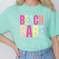 a woman wearing a green beach babe t - shirt