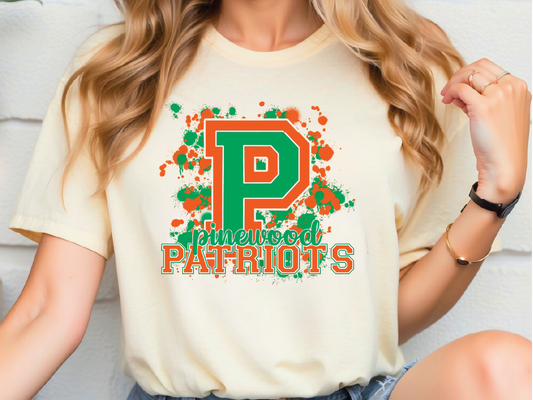 A person wearing a white t-shirt with a graphic design featuring a large letter "P" surrounded by splattered colors and the text "Pinewood Patriots".