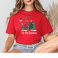 A woman wearing a red t-shirt with a Christmas tree design and the text "Tis the Season" is sitting against a white background.