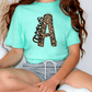 A person wearing a turquoise t-shirt with a leopard print design and gray shorts is sitting on the floor.