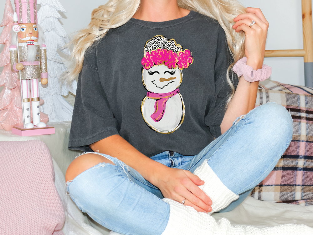 a woman sitting on a bed wearing a t - shirt with a snowman on