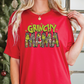 a woman wearing a grinchy mama t - shirt in front of a christmas tree