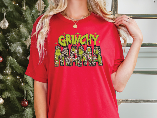 a woman wearing a grinchy mama t - shirt in front of a christmas tree