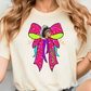 A woman wearing a white t-shirt with a colorful graphic design featuring a stylized Native American headdress and a pink bow.