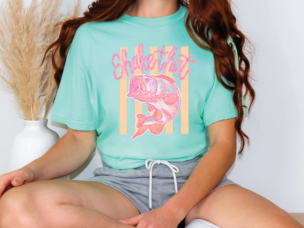 A person wearing a turquoise t-shirt with a fish graphic and the text "Shake that" printed on it.