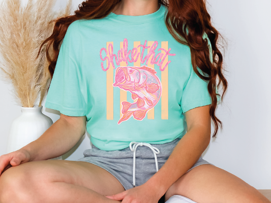 A person wearing a turquoise t-shirt with a fish graphic and the text "Shake that" printed on it.