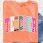 a bright orange t-shirt with the word "TEACHER" printed on it, along with colorful geometric shapes that spell out the word.