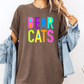A person wearing a brown t-shirt with the text "BEAR CATS" in colorful letters, along with a denim jacket, stands against a white background.