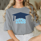 A woman wearing a gray t-shirt with a graphic of a graduation cap and the number "2026" printed on it.