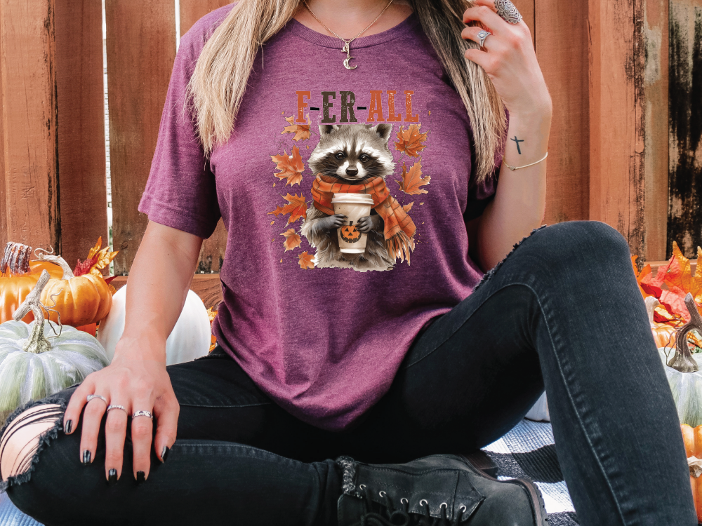 a woman sitting on the ground wearing a shirt with a raccoon on it