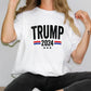 a woman sitting on a table wearing a trump t - shirt