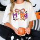 A woman wearing a white t-shirt with a Halloween-themed design is sitting on a couch, holding a pumpkin-shaped mug.