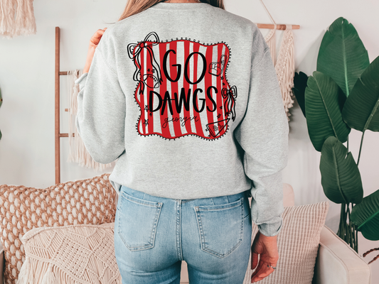 A person wearing a grey sweatshirt with a red and black graphic design on the back, standing in a room with a couch and plants.