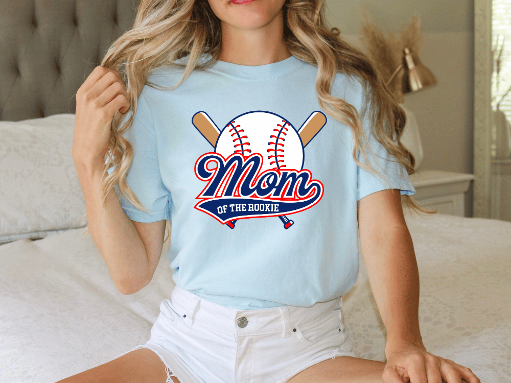 A woman wearing a light blue t-shirt with a baseball graphic and the text "Mom of the Rookie" printed on it.