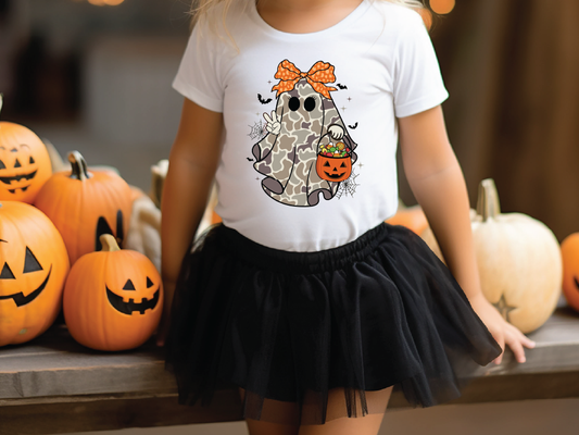 A young girl wearing a white t-shirt with a ghost graphic and a black tulle skirt stands in front of a display of Halloween pumpkins.