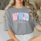 A woman wearing a gray t-shirt with the word "WHJD" printed on it, sitting on a bed.