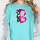 A woman wearing a turquoise t-shirt with a pink and black graphic design on it, standing against a white background.