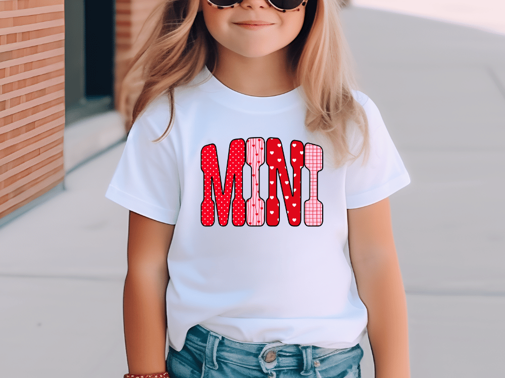A young girl wearing a white t-shirt with the word "MINI" printed on it, smiling at the camera.