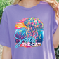 A person wearing a purple t-shirt with a colorful graphic of a jellyfish and the text "Seas the Day" printed on it.
