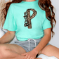 A person wearing a turquoise t-shirt with a leopard print design and gray shorts is sitting on the floor.