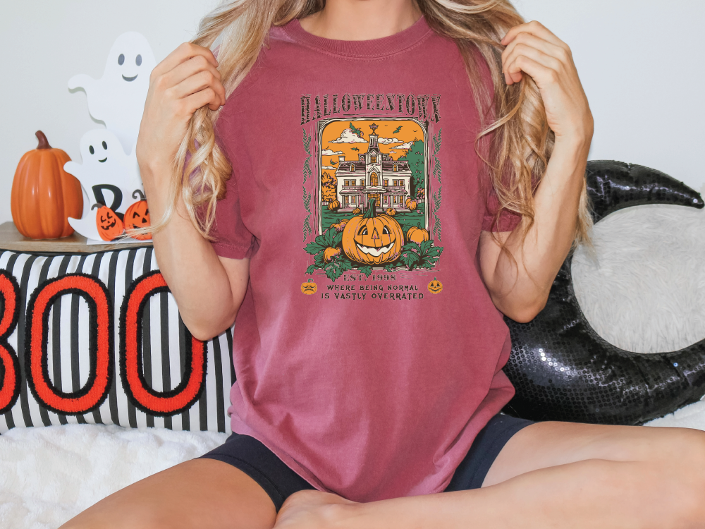 a woman sitting on a bed holding up a halloween t - shirt